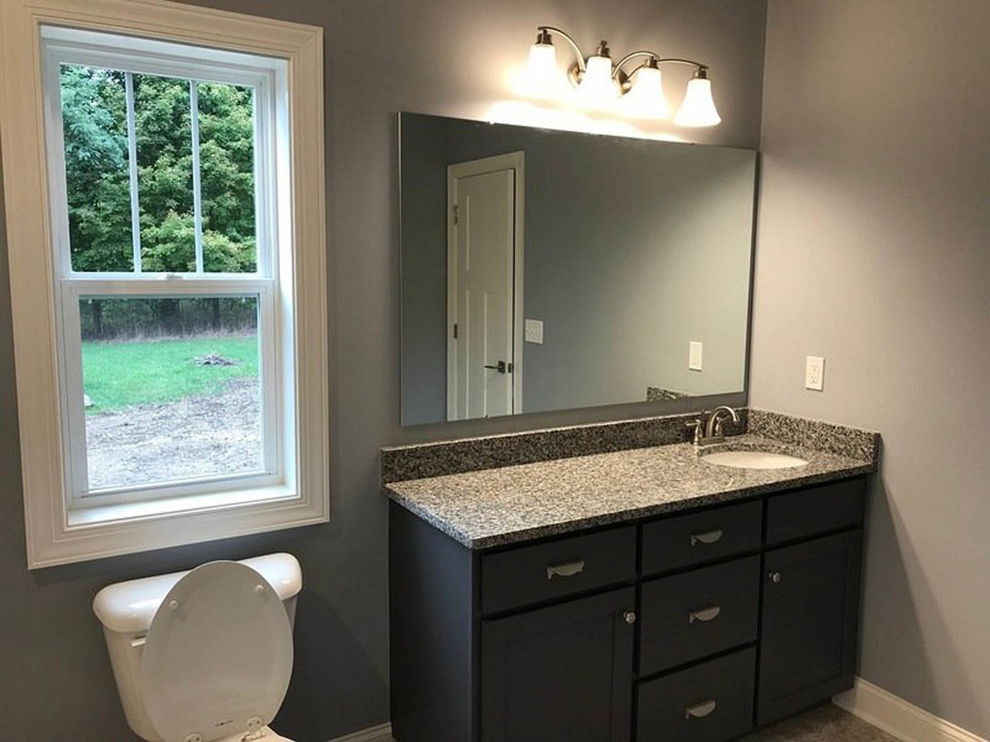 White tile bathroom featuring a rectangular mirror above a single sink vanity with chrome faucet, toilet with lid up, three-light fixture mounted above the mirror, window