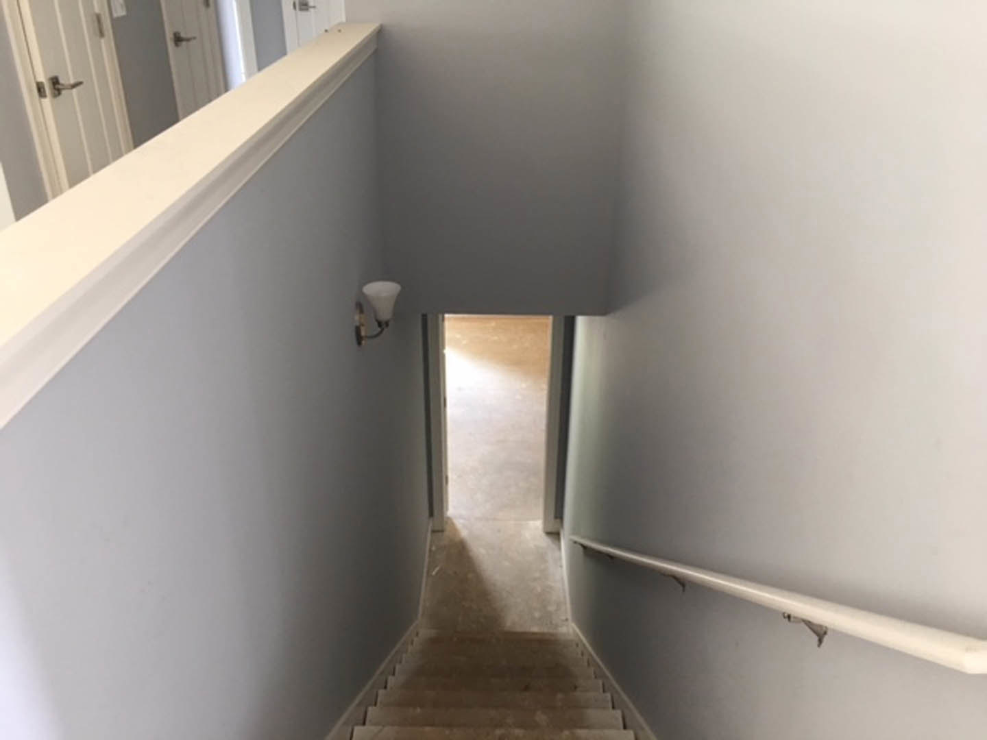 Wood staircase with white risers and trim, leading to a hallway with plaster walls, white door opening to a room, and brushed metal door handle visible in foreground