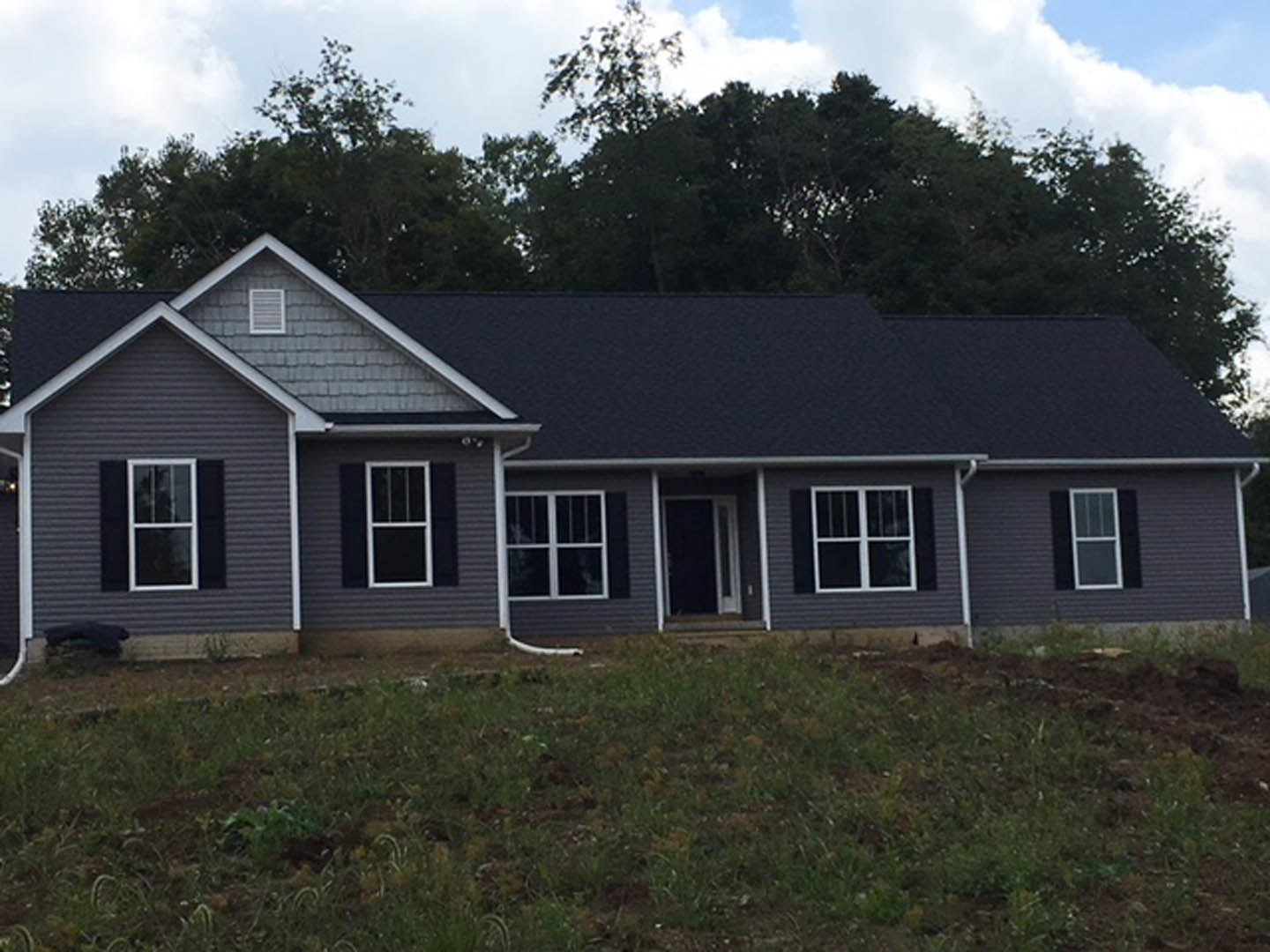 Two-story house with black roof, white siding, white-framed windows, and expansive green lawn under partly cloudy sky