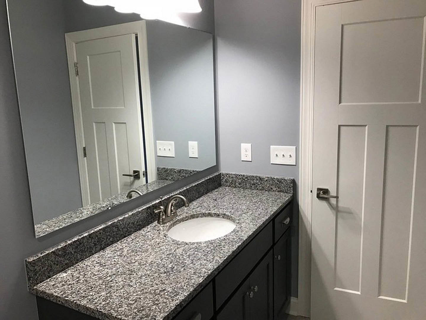 Granite countertop vanity with undermount sink, large framed mirror above, tile backsplash, and chrome faucet in a modern bathroom
