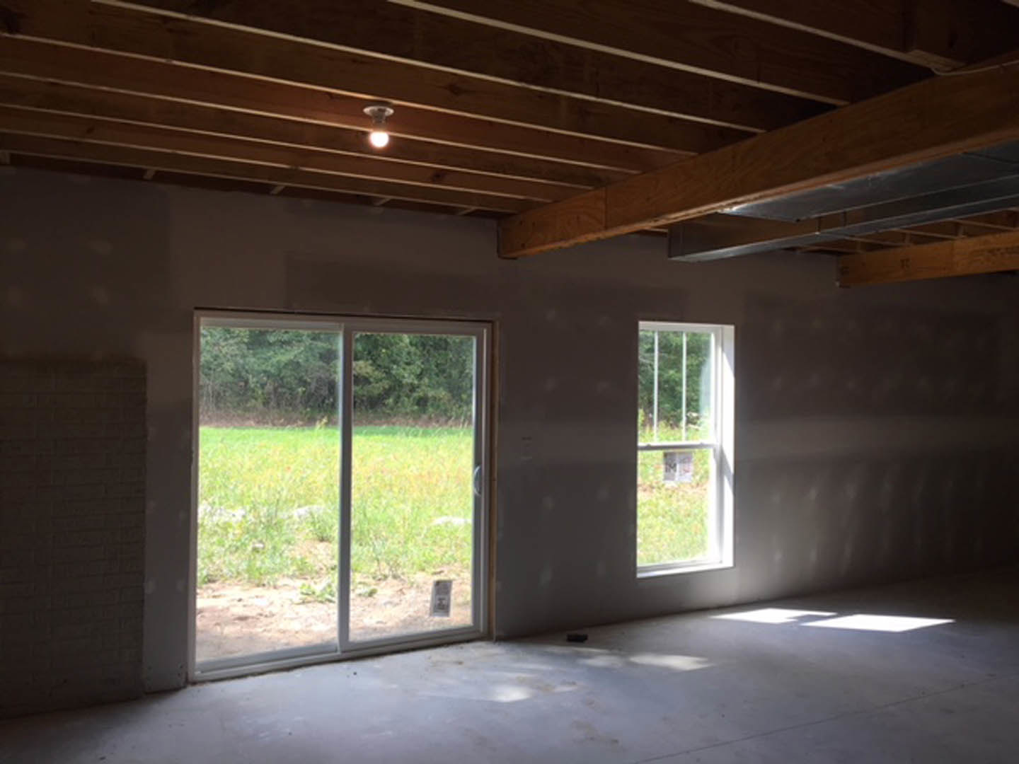 Modern room featuring a glass door and large windows, white walls, light wood flooring, ceiling light fixture, and views of grassy field and outdoor signage.