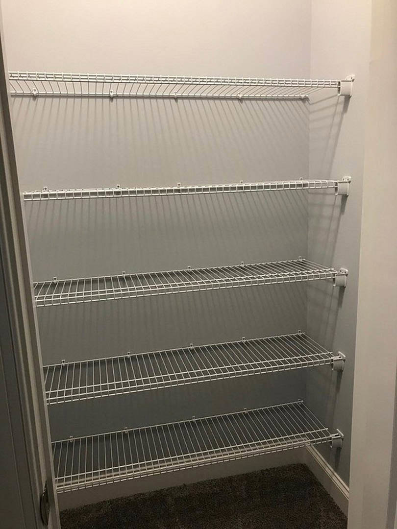 Empty closet with gray walls, white wire shelving, and black carpet with a white floor vent