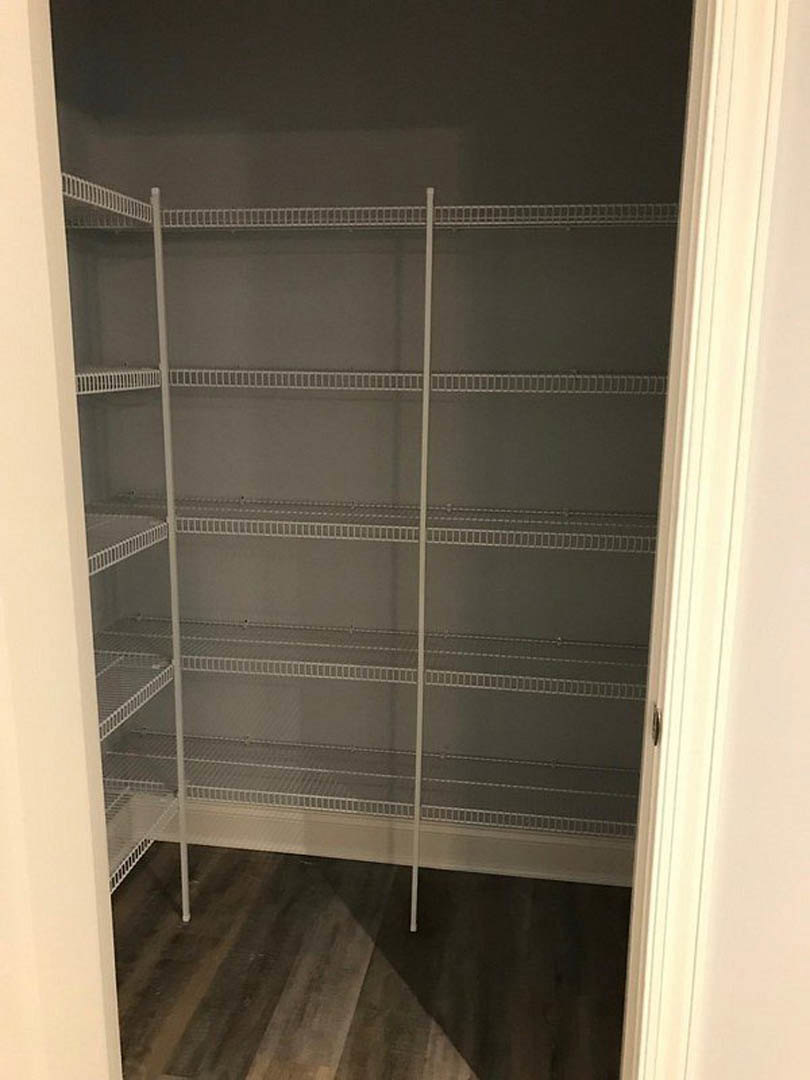 Closet with white metal shelving, dark wood flooring, white curtain, and white pole beneath a grey ceiling