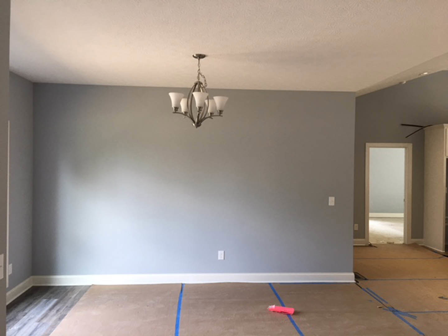 Chandelier with white shades hanging from ceiling, brown carpet covering floor, white walls, wood flooring near doorway