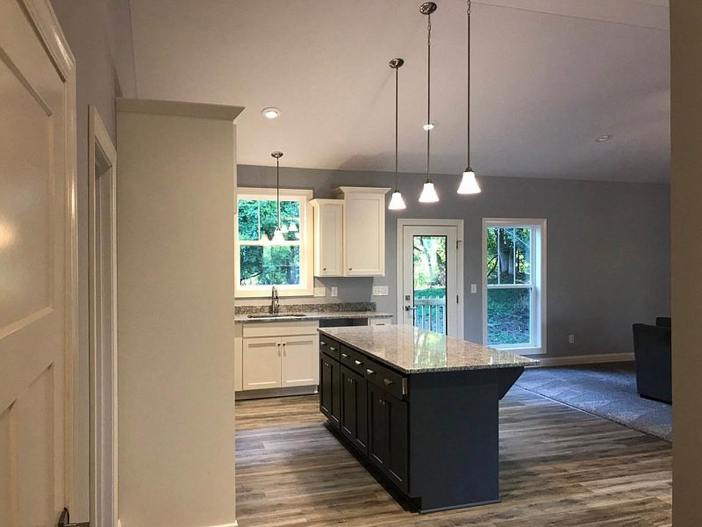 Kitchen with black island featuring granite countertops and drawers, wood flooring, white cabinetry, window with white frame, white door with window, and white-shaded light