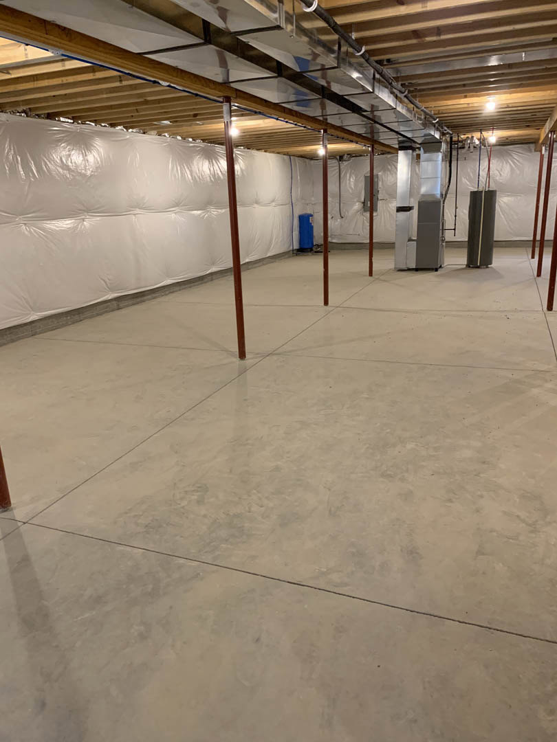 Concrete floor and white wall with exposed metal poles in an empty basement interior