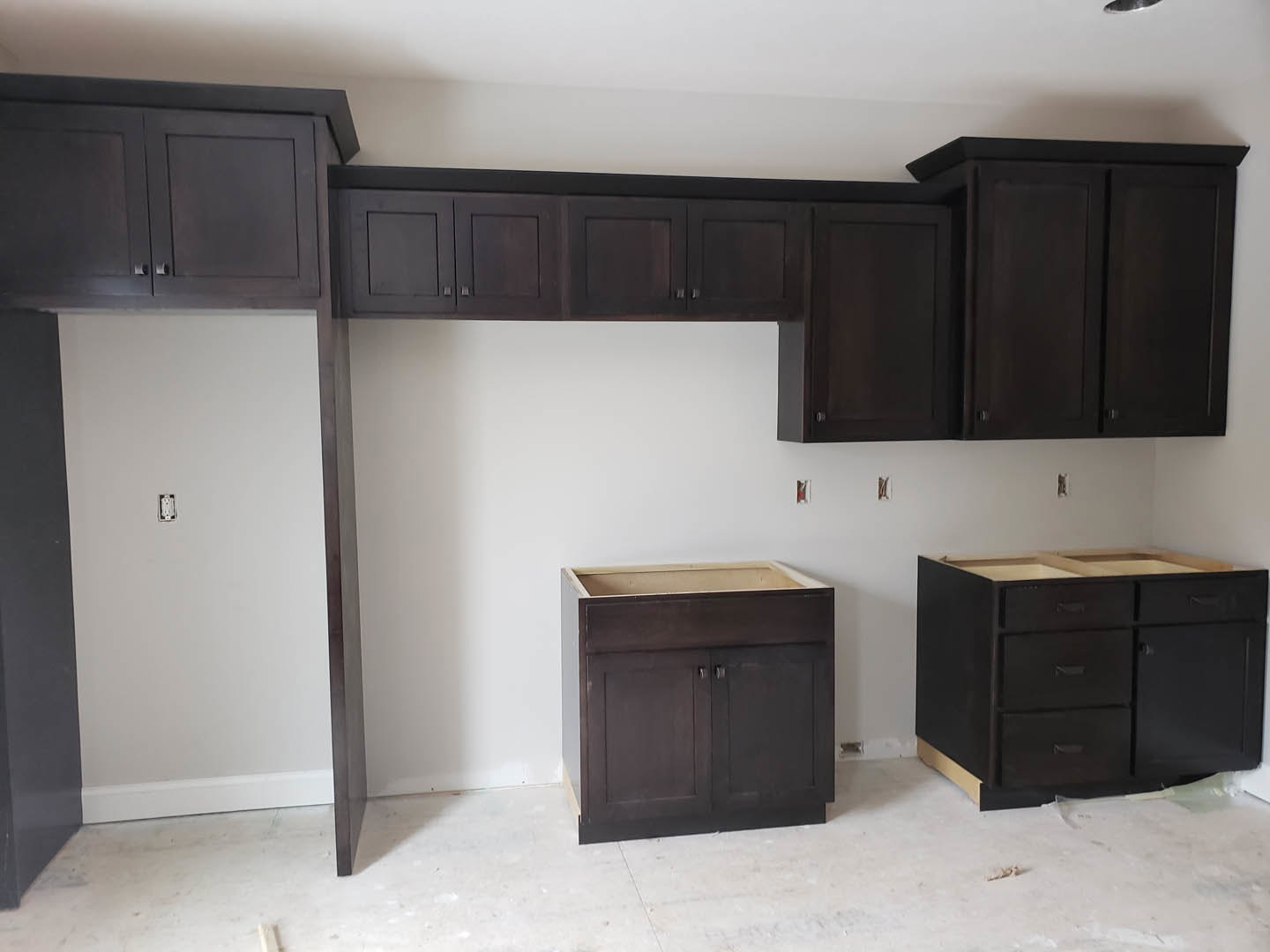 Kitchen featuring dark wood cabinets, white tile flooring, black door, upper cabinets against a white wall, and black drawer pulls