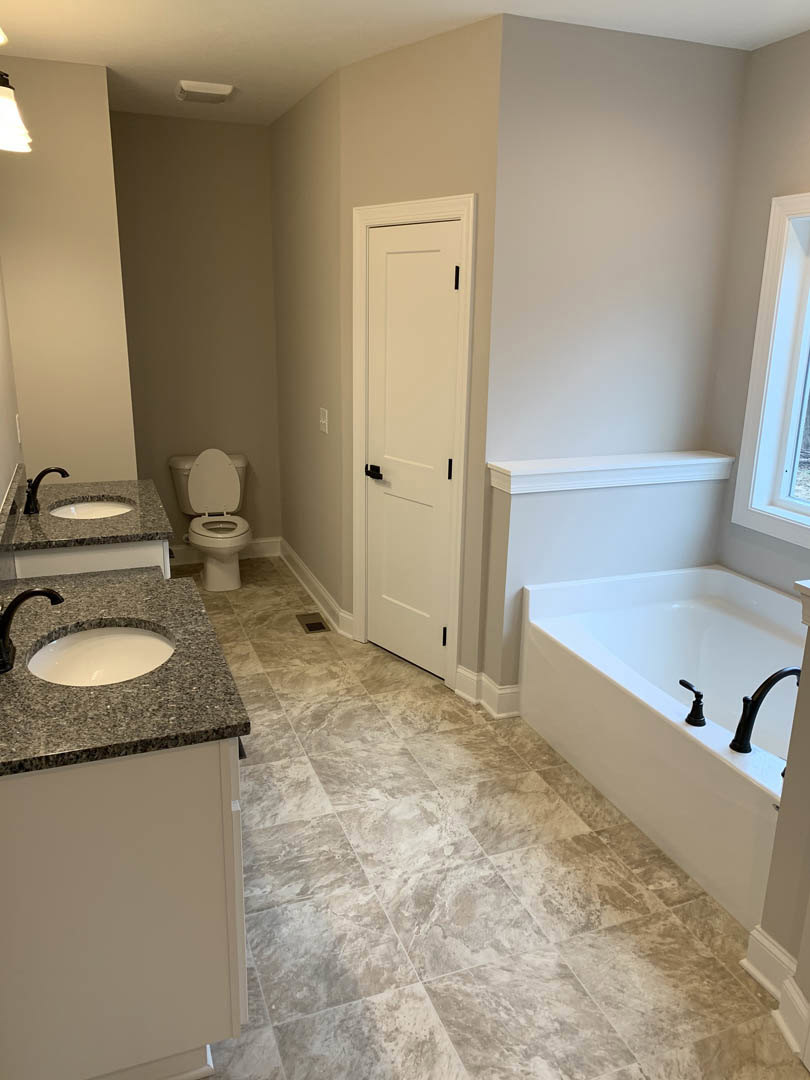 Bathroom with marble tile flooring, marble-edged white sink, freestanding bathtub with chrome faucets, toilet with seat up, white door with black handles, window close-up.