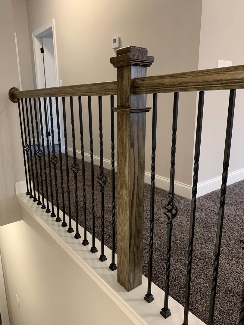 Black metal railing and wooden post on staircase, white wall, door with black handle