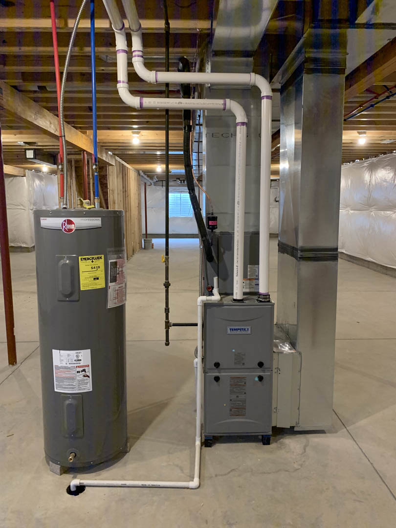 Grey metal boiler and heater units installed on a concrete floor, with a yellow caution sign and visible aluminum surfaces in a utility room.