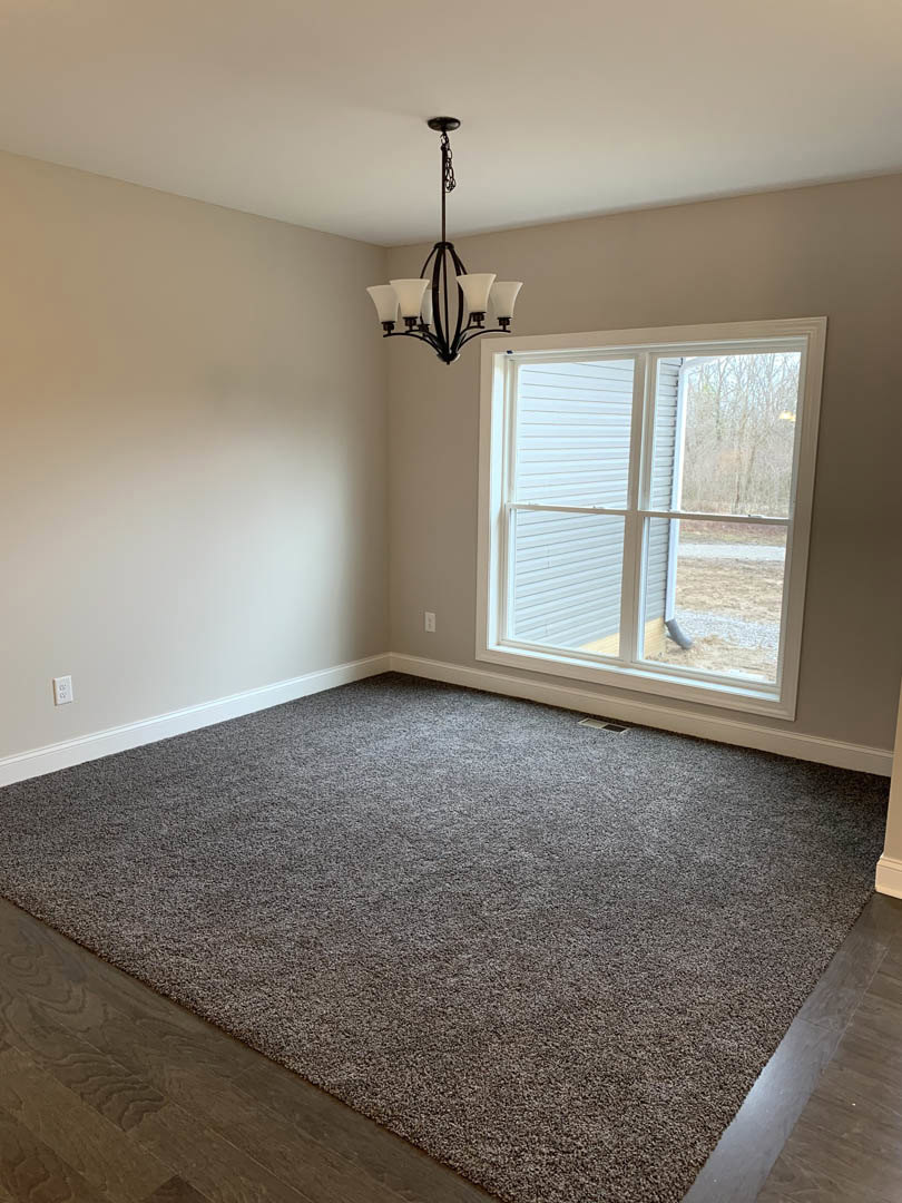 Bright room with large window overlooking yard, ornate chandelier hanging from plaster ceiling, neutral walls with crown molding, laminate wood flooring, carpeted area, window