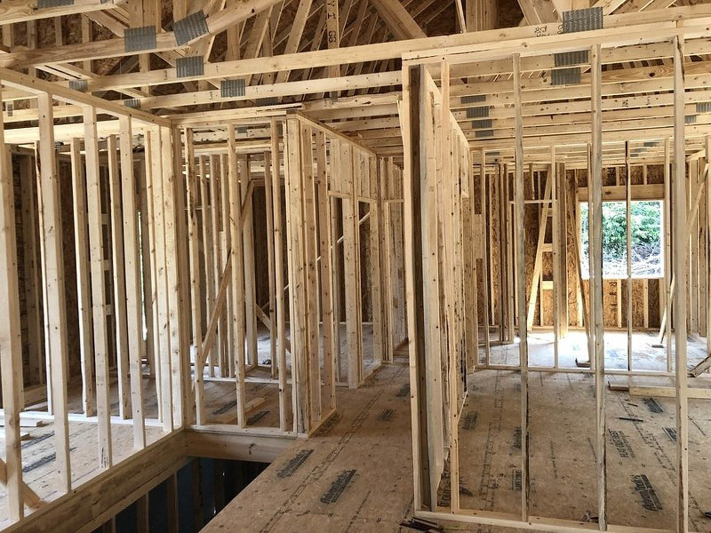 Exposed wood framing and beams inside a house under construction, unfinished walls and ceiling with visible lumber