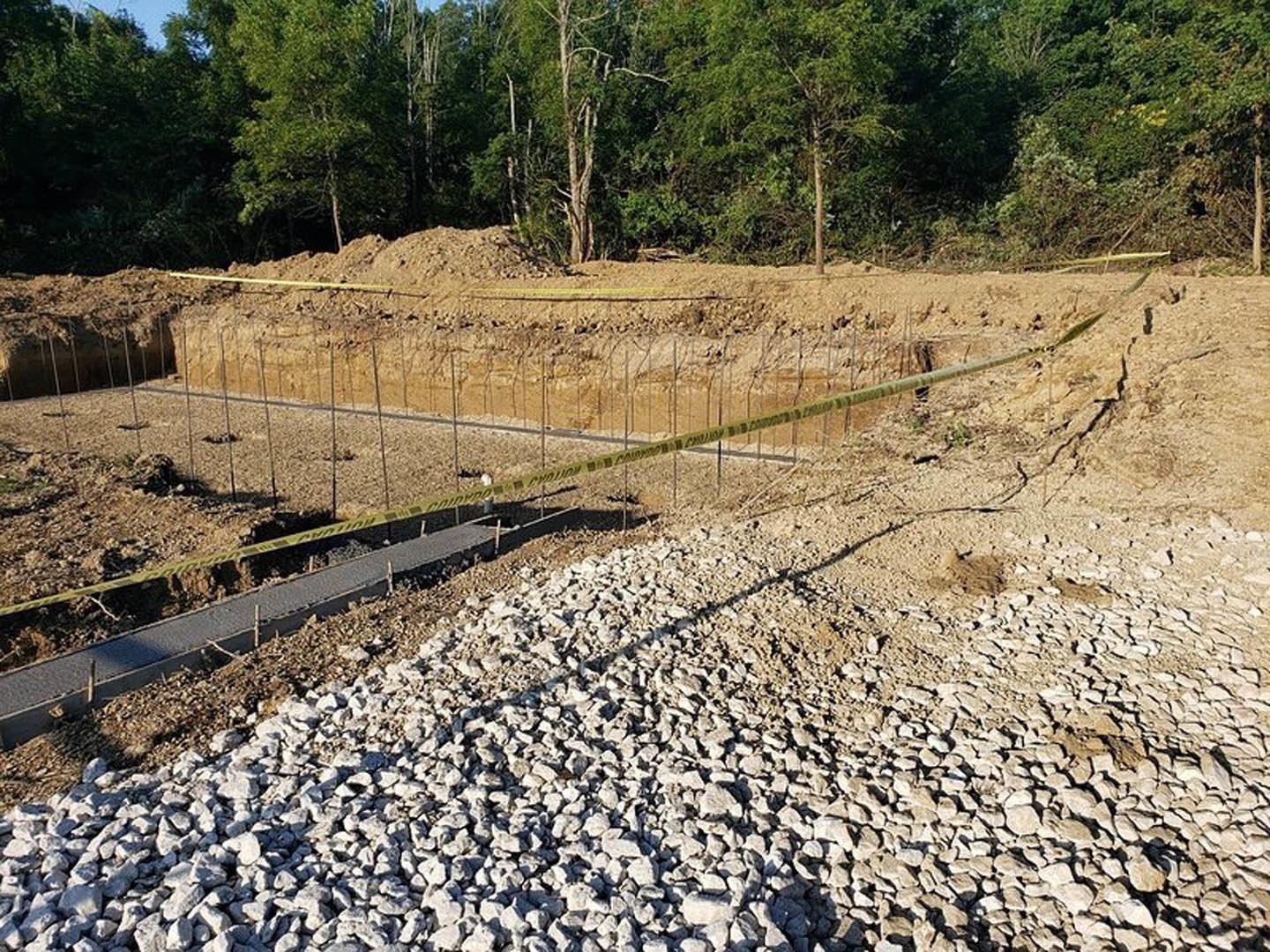 Gravel and rocks scattered across a construction site with a partially built bridge, yellow caution tape, and a tree in the background