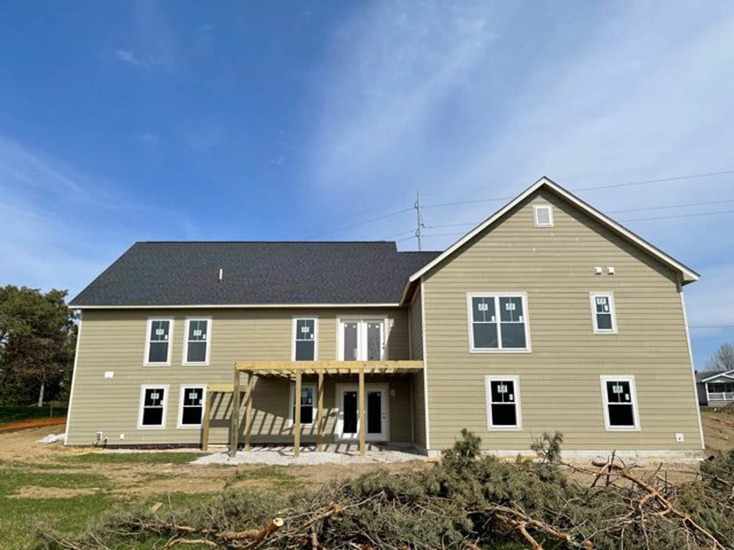 Two-story house under construction with exposed wooden framing, covered front porch, white-framed windows, and light-colored siding; cloudy sky overhead