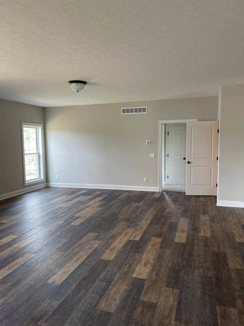 Hardwood floor room with white walls, black hardware on white door, white-framed window, and modern ceiling light fixture