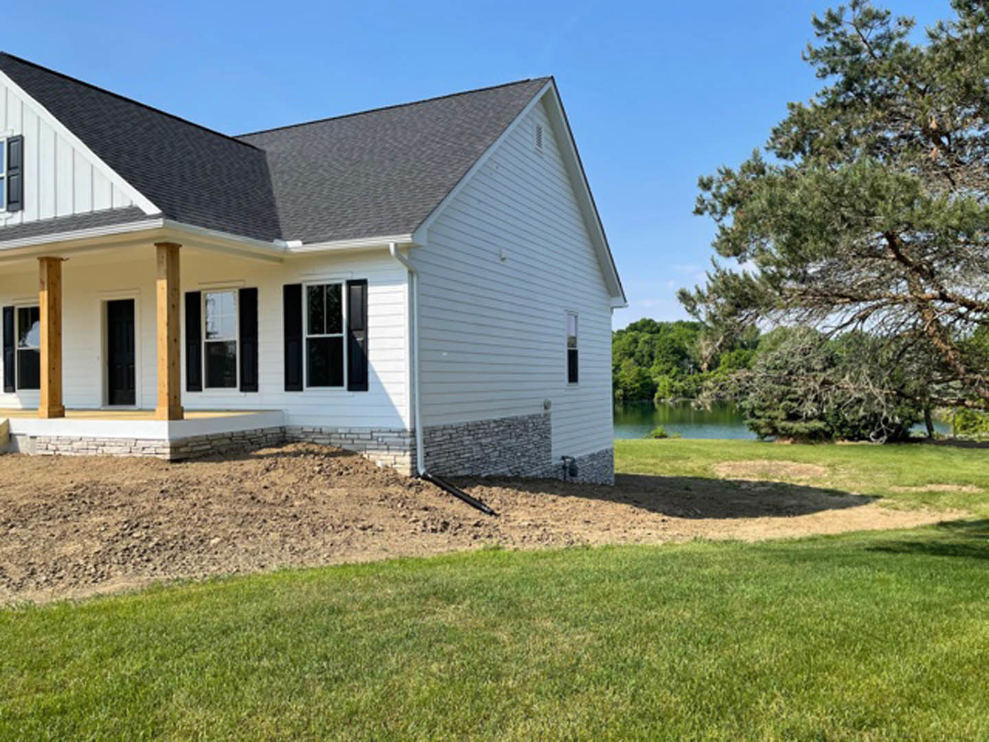 White house with black roof and shutters, large grassy yard, mature tree with green leaves, front porch, multiple windows