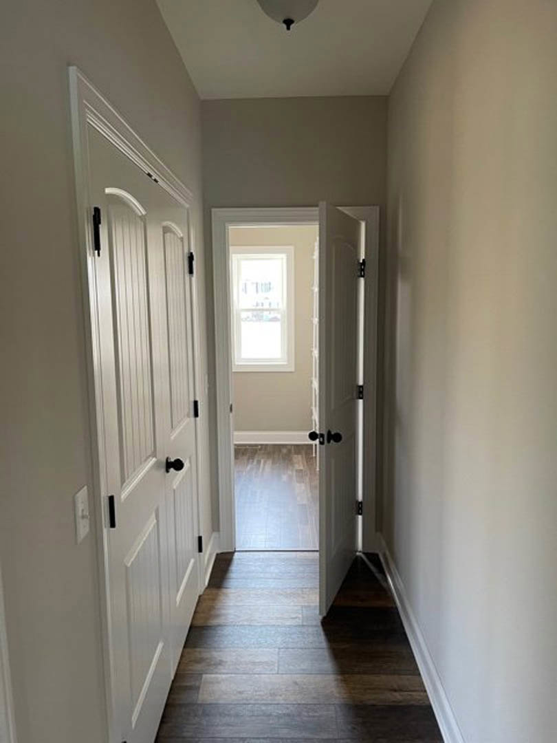Hallway with white paneled doors, black handles, dark hardwood flooring, white framed window, and white baseboards