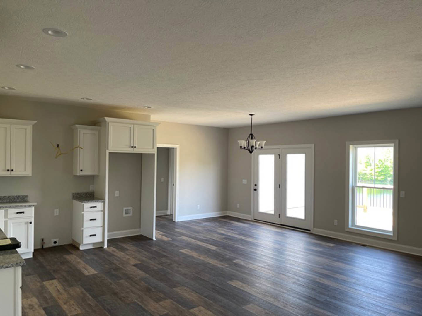 Open kitchen with wood flooring, white shaker cabinets, black hardware, glass-paneled double doors, large window with railing, and modern chandelier