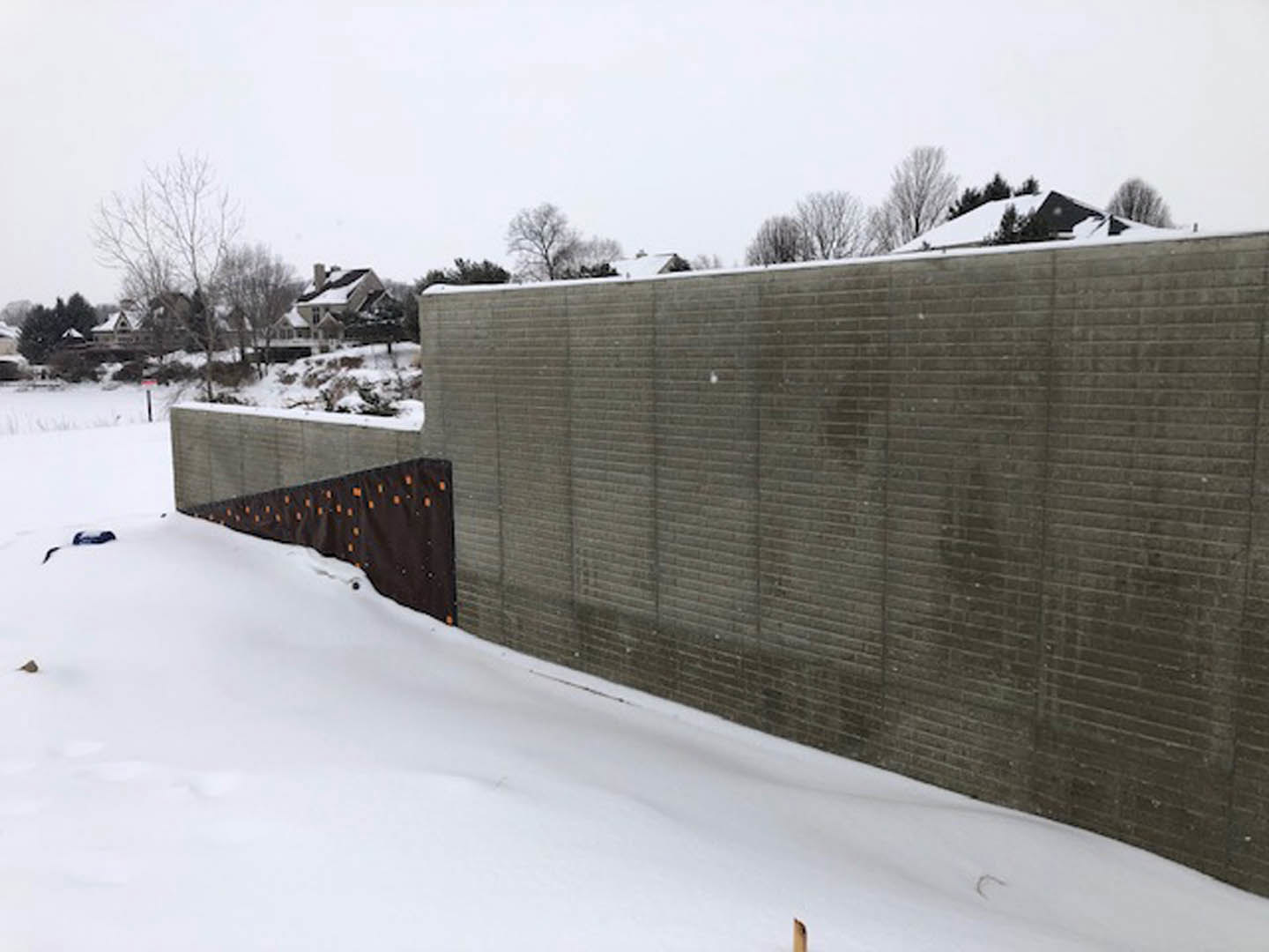 Snow-covered ground and trees surrounding a modern house with a fence and gate, winter sky overhead