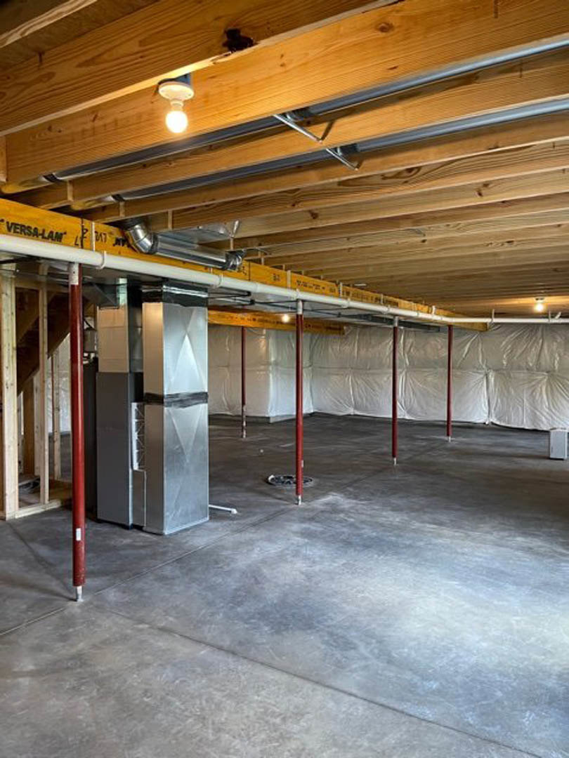 Basement room with exposed steel beams, white ceiling panels, concrete floor, red support poles, and a single light bulb mounted on the wall.