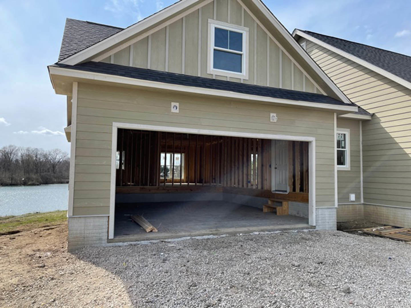 Two-story house with attached garage, white-framed windows, light-colored siding, covered porch, paved driveway, and mature trees in the background