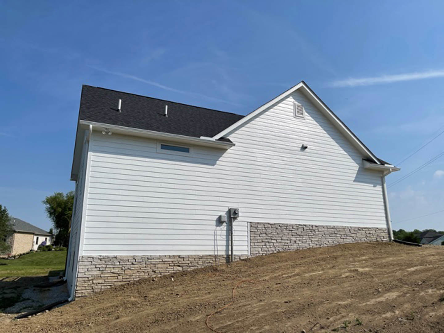 White siding house with black shingle roof, surrounded by green lawn and mature trees under a partly cloudy sky