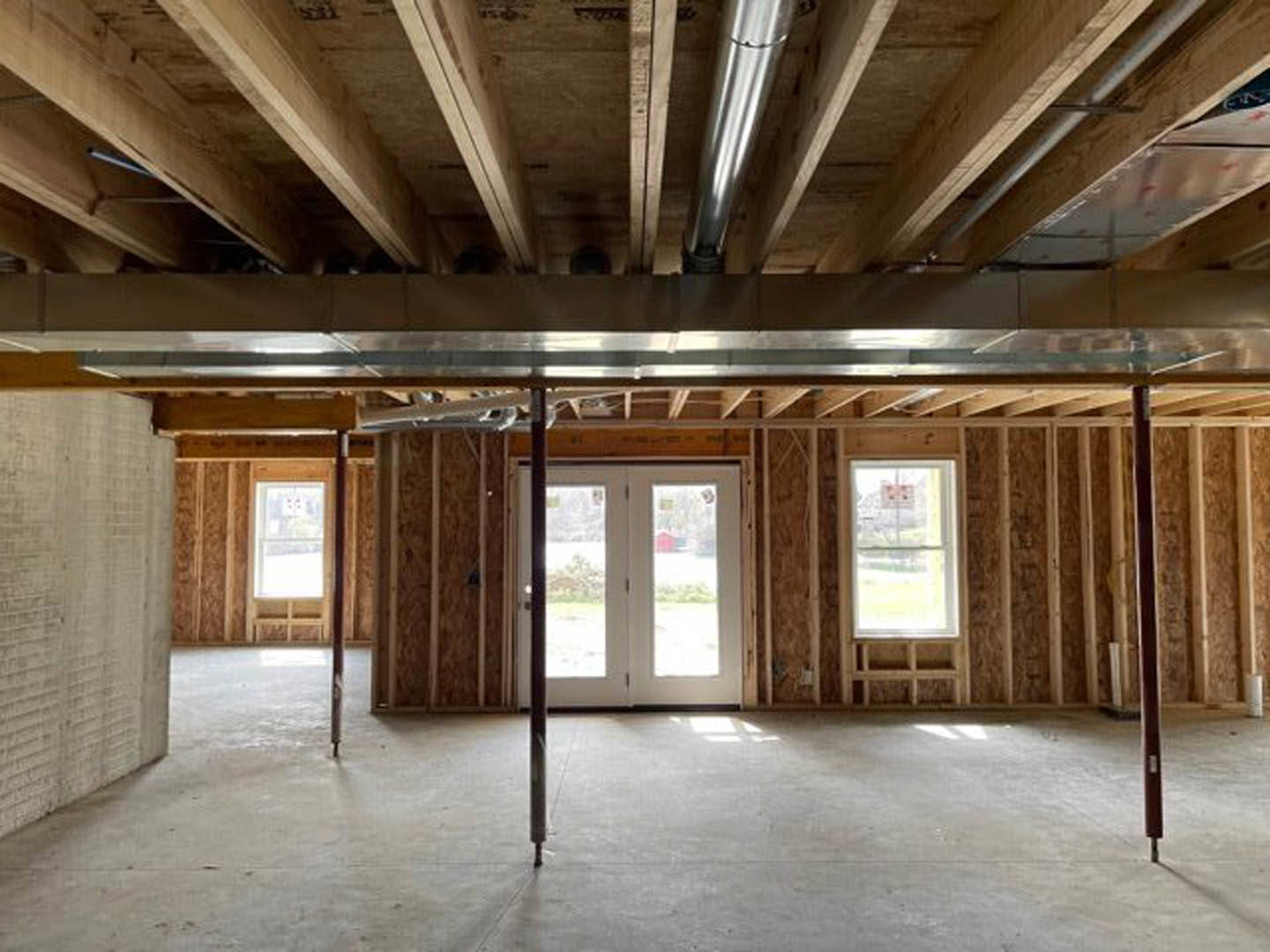Wood plank ceiling with exposed beams, double glass-paneled doors, large windows, light-colored walls, and hardwood flooring