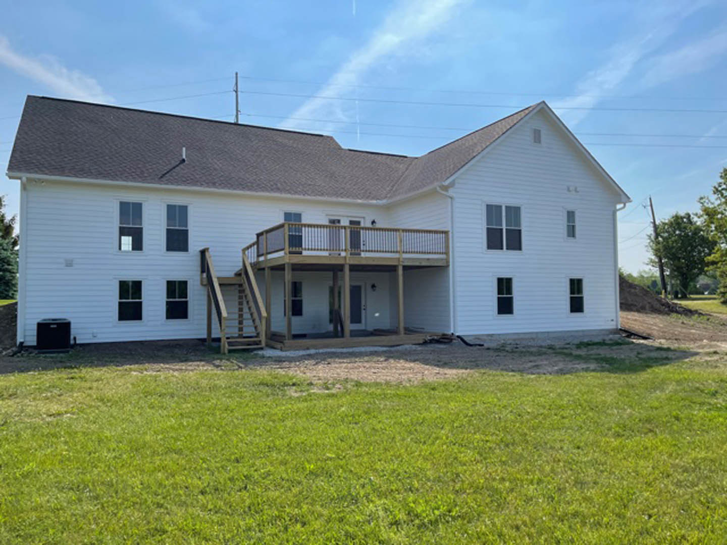 White siding house with elevated wooden deck, expansive green lawn, large windows, and cloudy sky in background