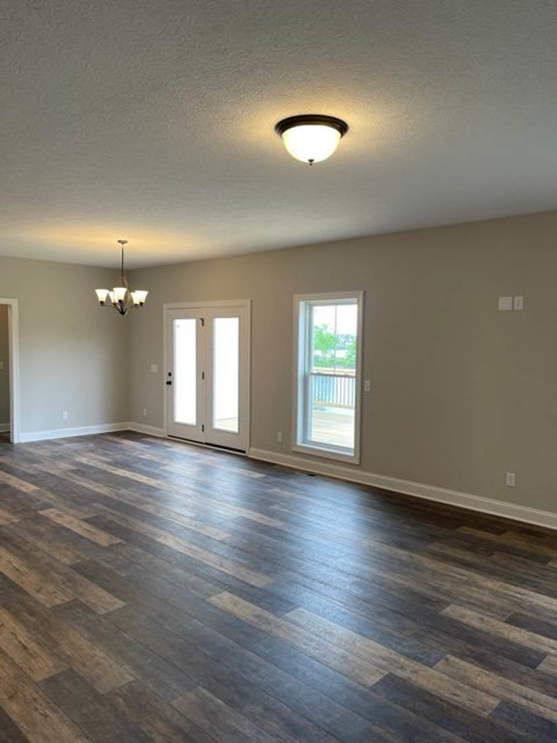 Hardwood floor room with white walls, glass-paneled door, large window overlooking exterior railing, and ceiling-mounted chandelier with white shades
