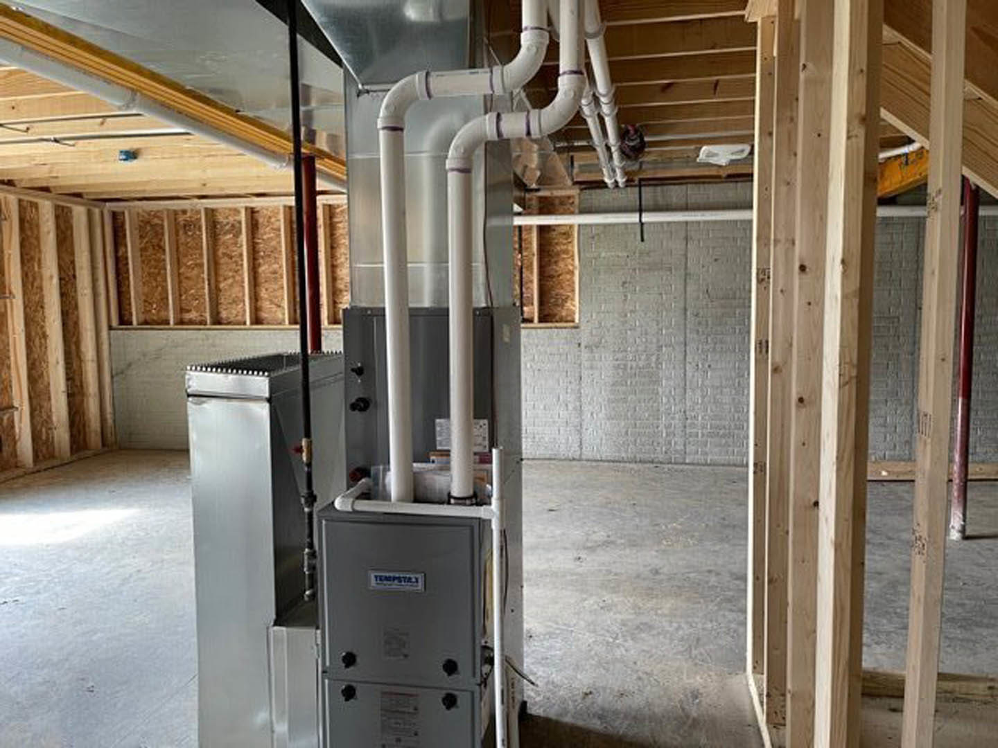 Exposed aluminum pipes and beams run along a wall and ceiling in a utility room with composite flooring; a close-up lamp and a grey rectangular fixture with black knobs are