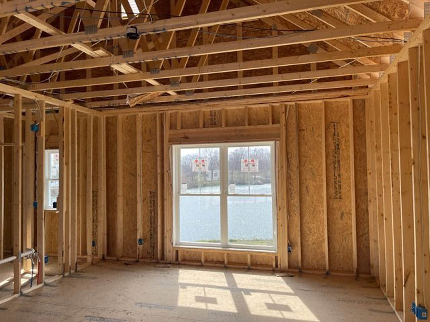 Sunlit room with exposed wood ceiling beams, large window, concrete floor, and visible window shadows.