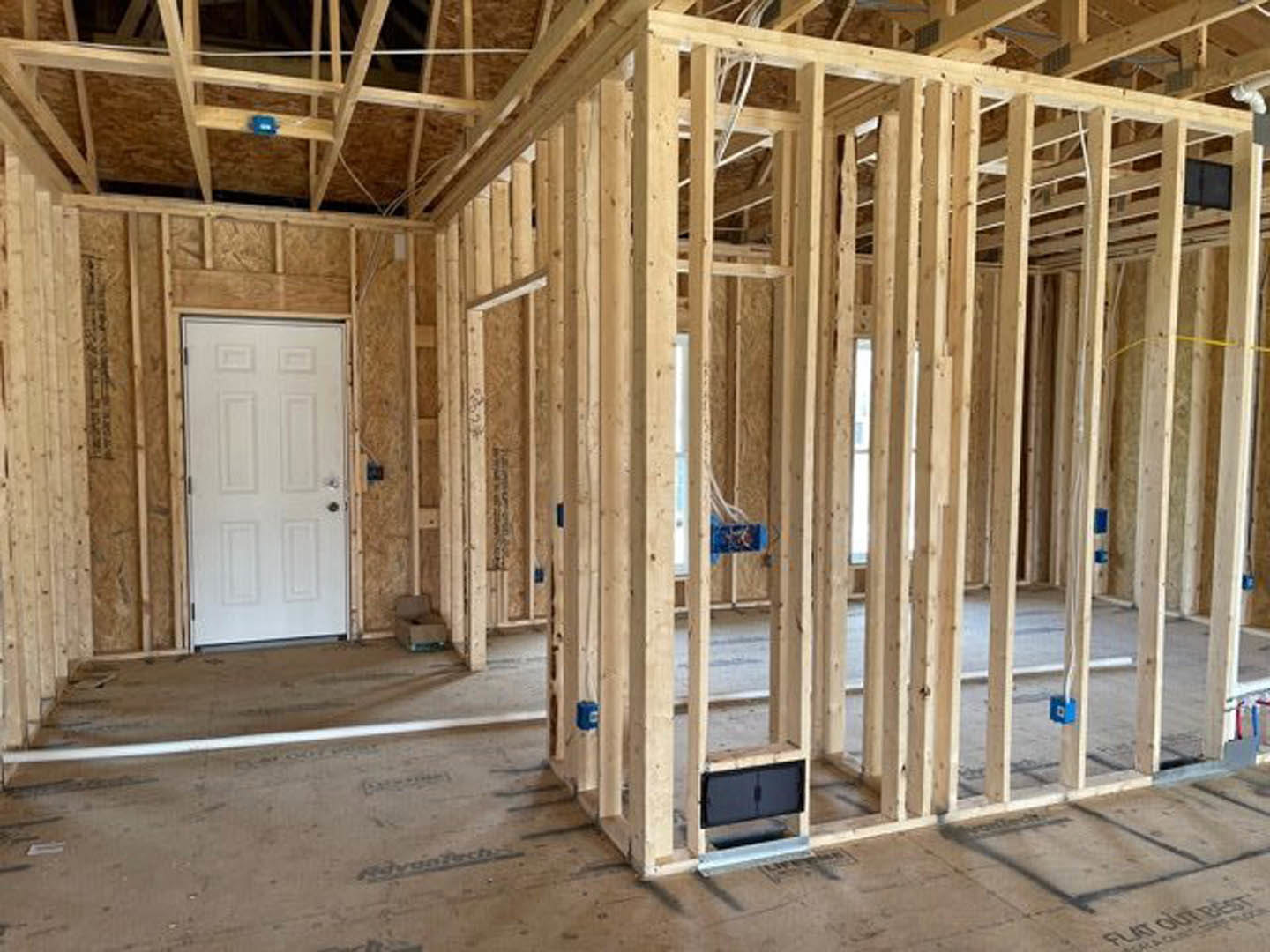 Wood-framed room under construction with exposed beams, white door set in wooden frame, unfinished floors, and visible insulation