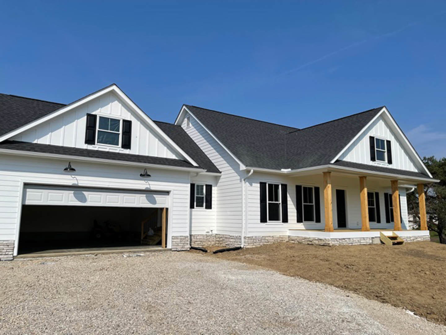 Modern house exterior with light siding, white-framed square window, attached garage partially shadowed by a parked car, gravel driveway, and white pipe along the ground