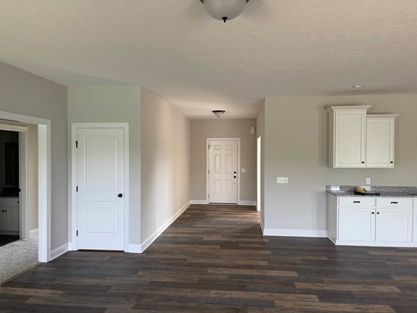 White paneled doors with black knobs, dark wood flooring, white walls, white kitchen cabinetry and drawers, ceiling light fixture