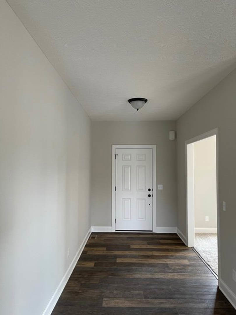 Hallway with dark wood flooring, white walls with black trim, white door featuring black knobs, ceiling light fixture