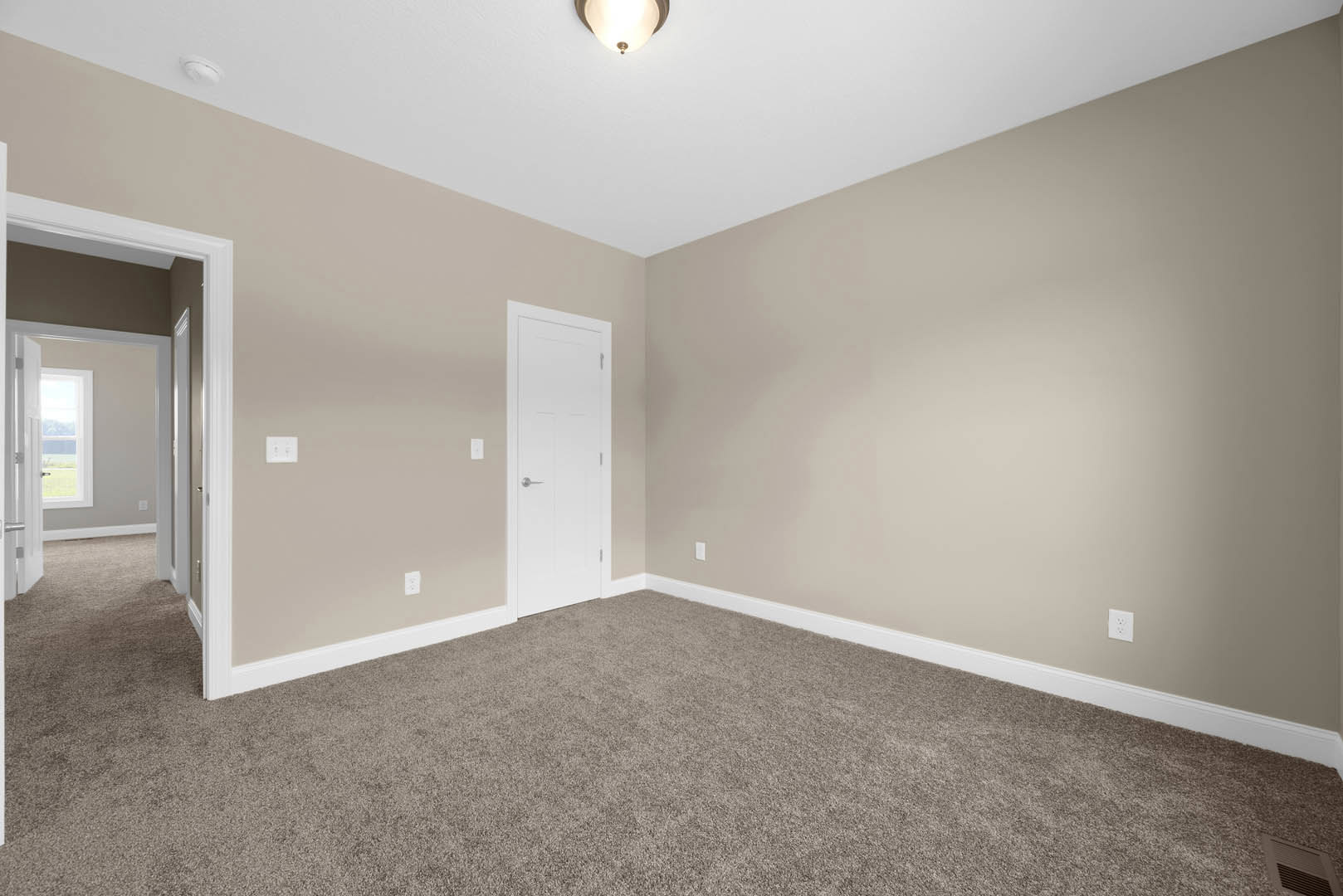 White paneled door with silver handle, beige carpet flooring, white plaster walls, ceiling light fixture, and wall vent in a residential interior room