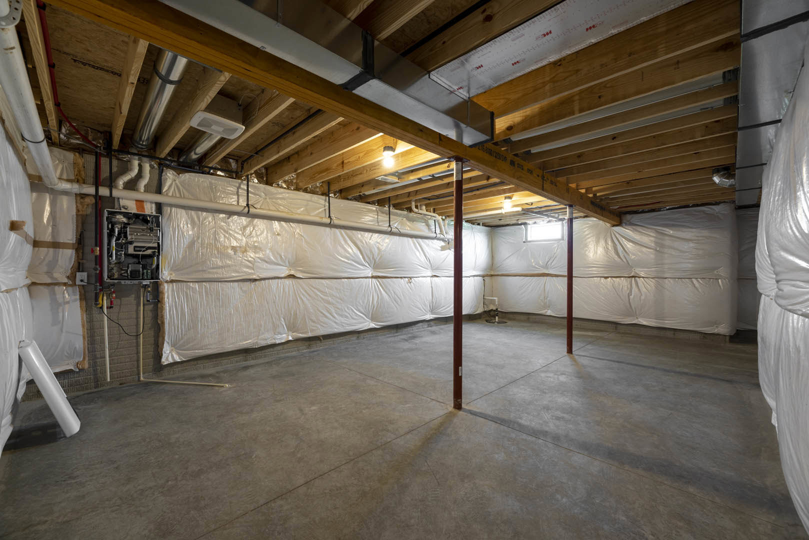 Basement room with concrete floor, exposed metal pipe and pole, white plastic covering on ceiling and walls, unfinished surfaces.