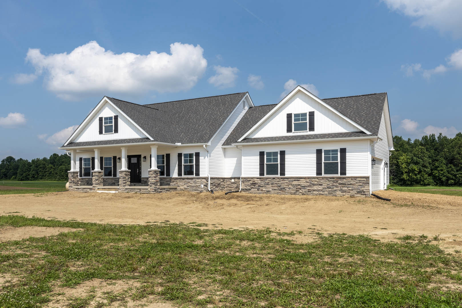 White siding house with black front door, white framed windows, gray shingle roof, gutter, and dirt yard under blue sky