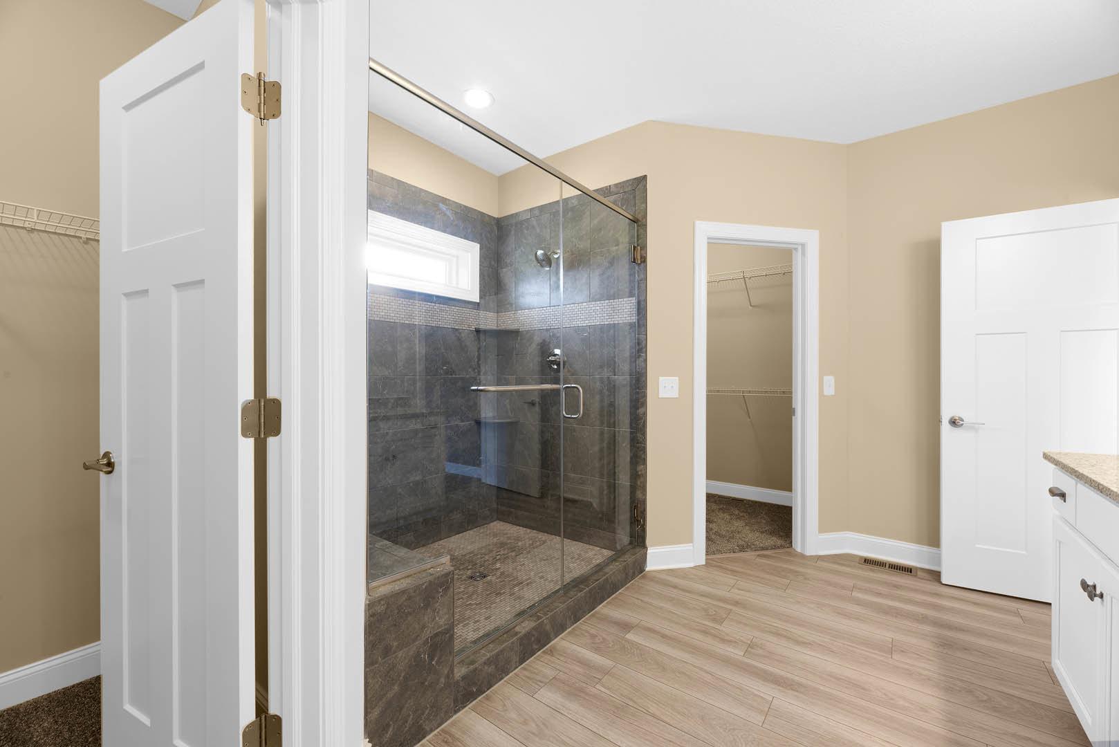Bathroom featuring a glass shower enclosure, wood flooring with a small carpet, white door with silver handle and white frame, window in shower area, brown door hinge on white