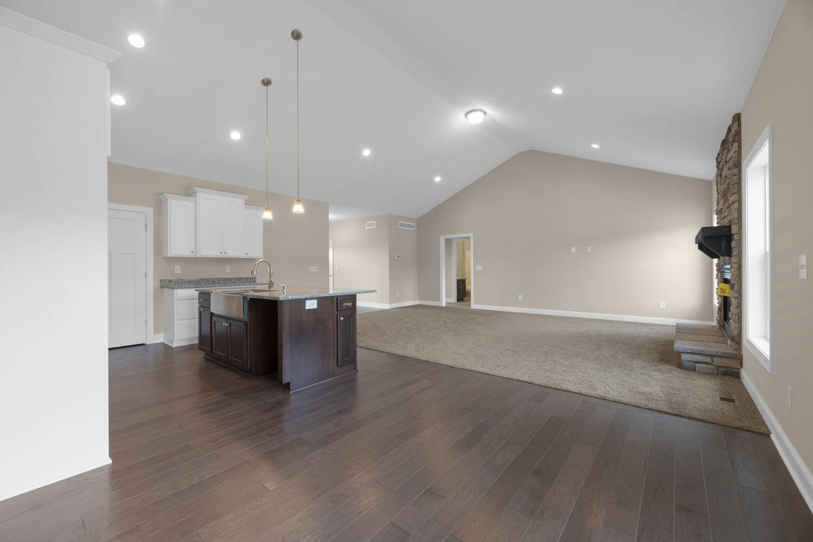 Spacious open concept interior featuring a kitchen island with sink, hardwood flooring transitioning to carpeted area, white cabinetry along the wall, and a white door with