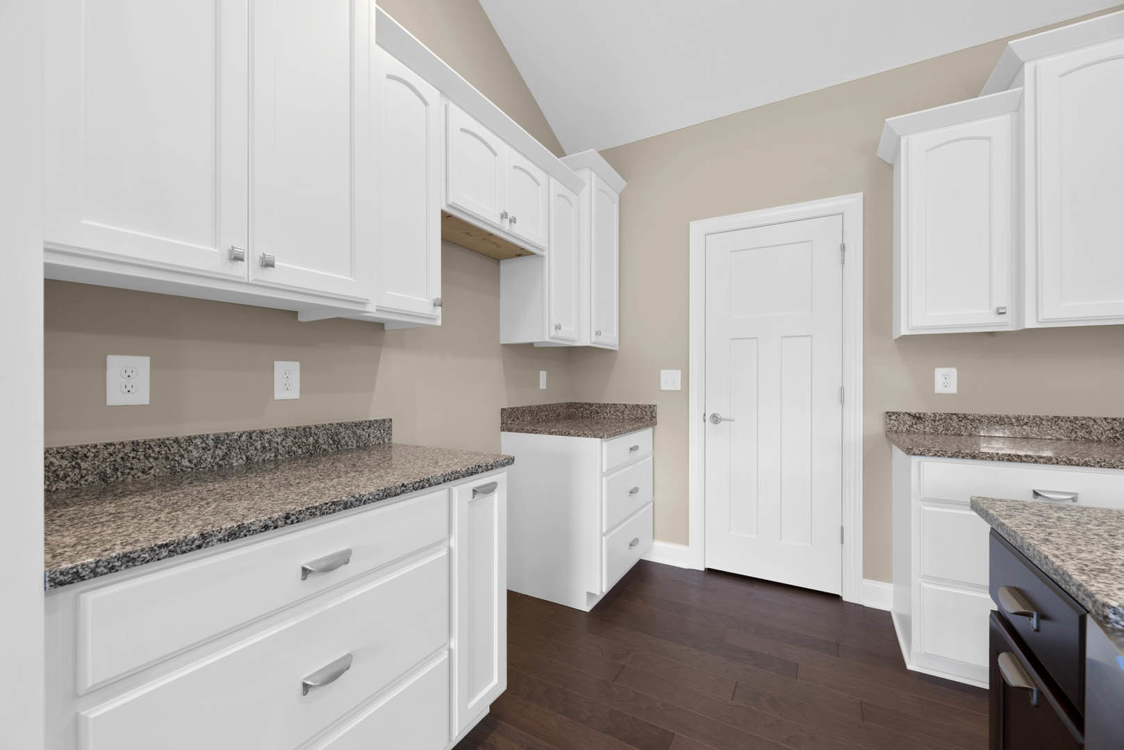 White kitchen with granite countertops, white cabinets, stainless steel hardware, white door with silver handle, knife on countertop, white outlet on wall, drawers beneath counter