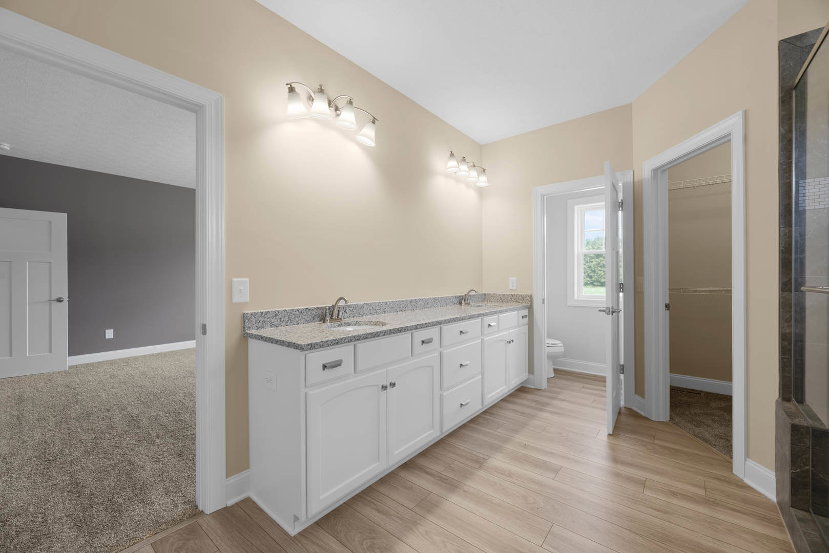 Bathroom with double vanity, white sinks, wood plank flooring, light gray cabinetry, quartz countertop, silver faucets, and white paneled door with chrome handle