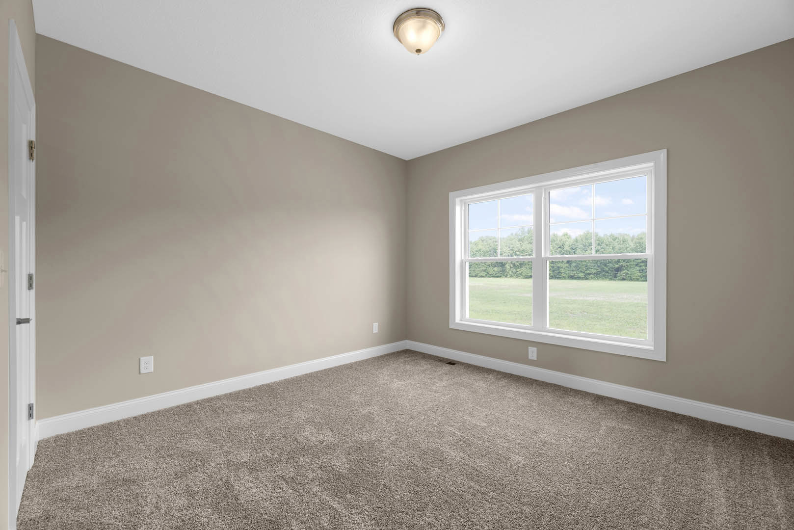 Carpeted room with white walls, large window overlooking grassy field, ceiling-mounted light fixture, white door with metal hinge