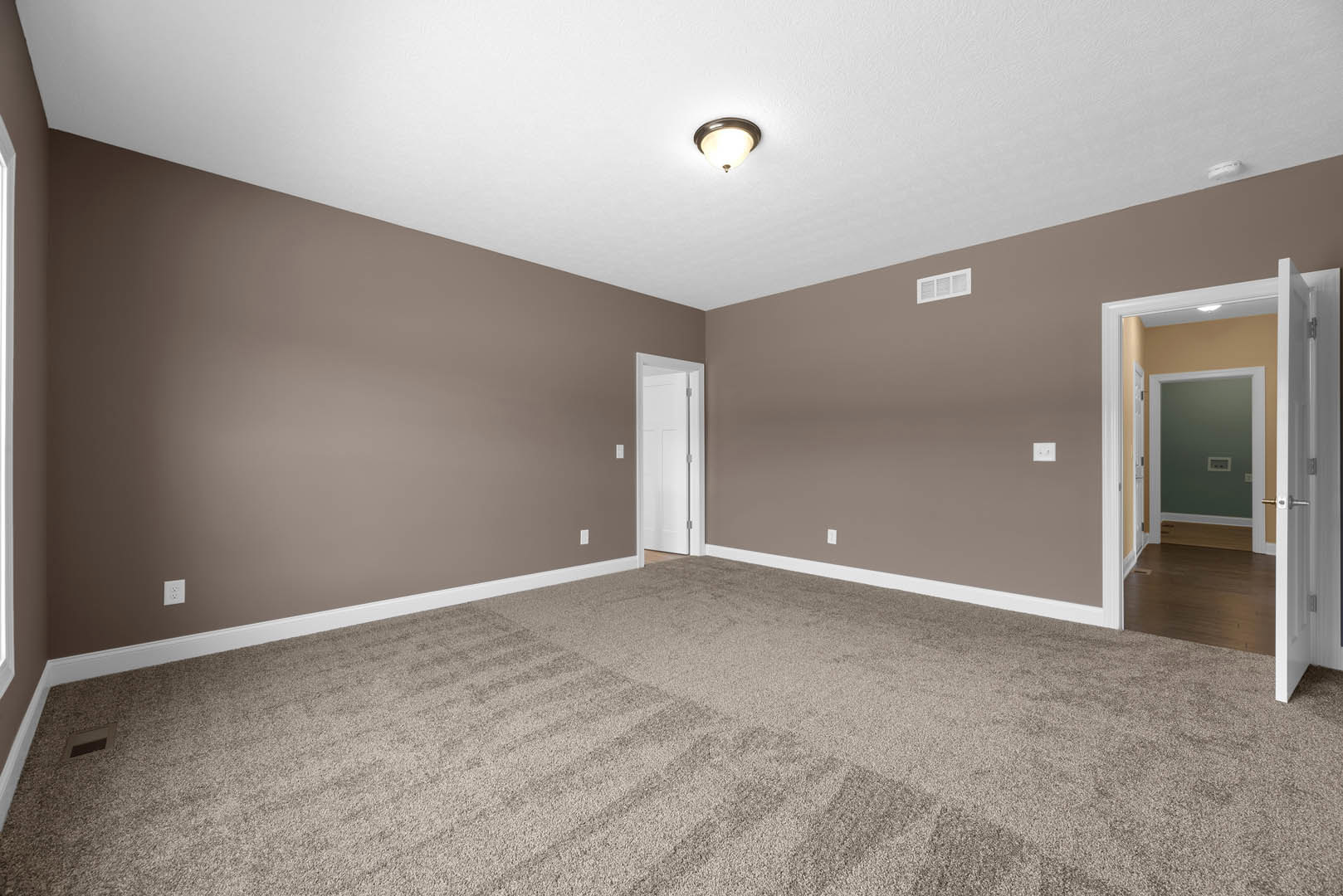 Brown carpeted room with brown painted walls, white ceiling vent, white door featuring a cross detail, and ceiling-mounted light fixture