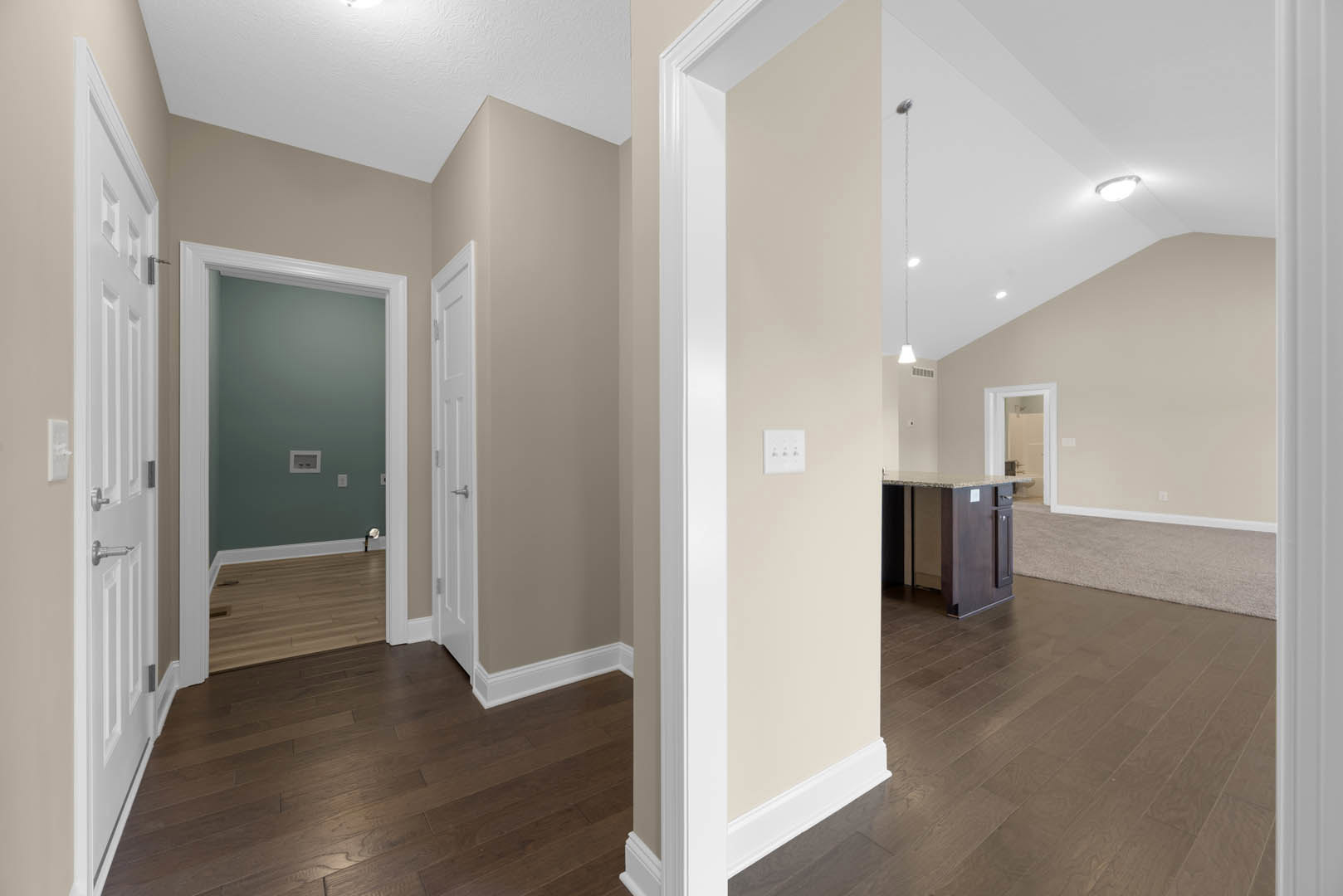 Hallway with light wood flooring, white baseboards, and a carpet runner leading to a kitchen featuring a marble-topped island; three-button black and white light switch on the wall