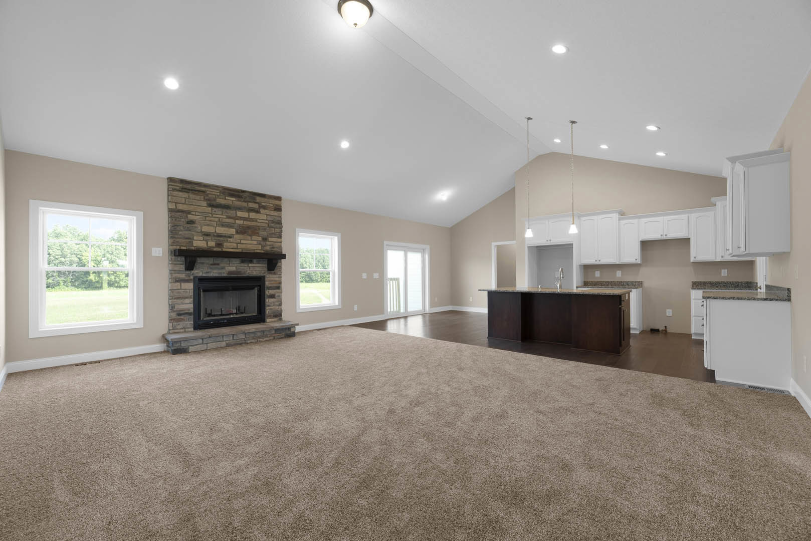 Spacious living room featuring a glass-door fireplace, marble kitchen countertop, carpeted floor, cabinetry, and large window overlooking a green lawn