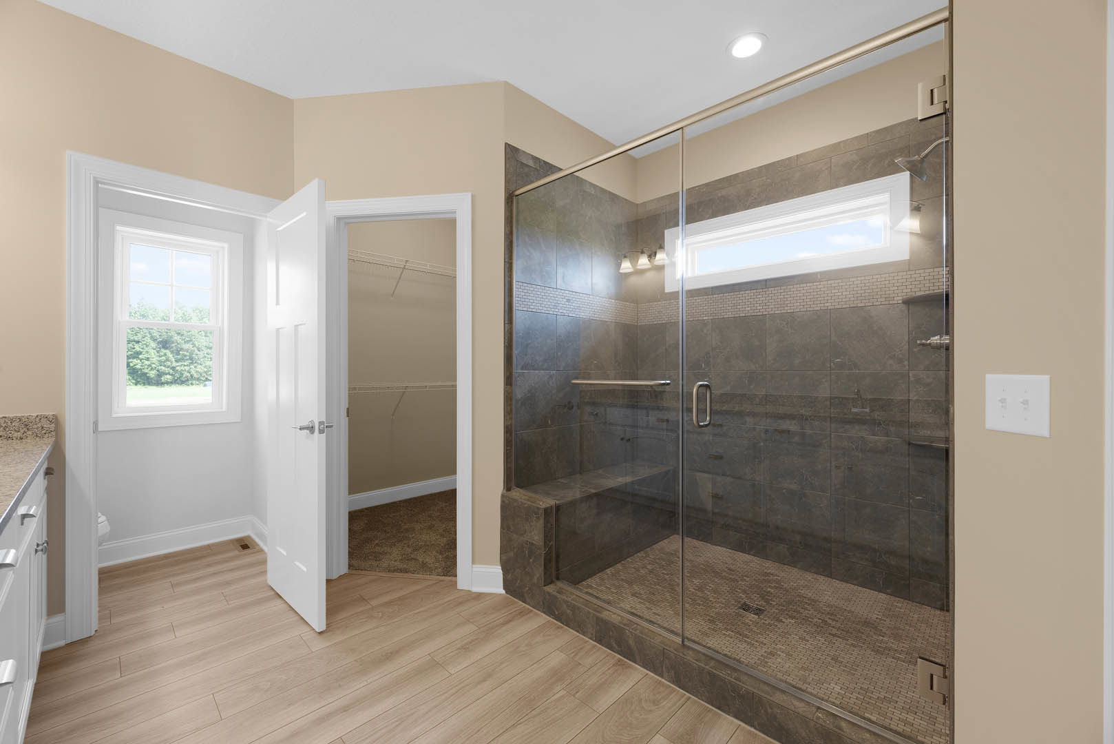 Bathroom featuring a glass shower enclosure, wood flooring, white door with matching frame, large window overlooking trees, and white wall outlet with black and white markings on a