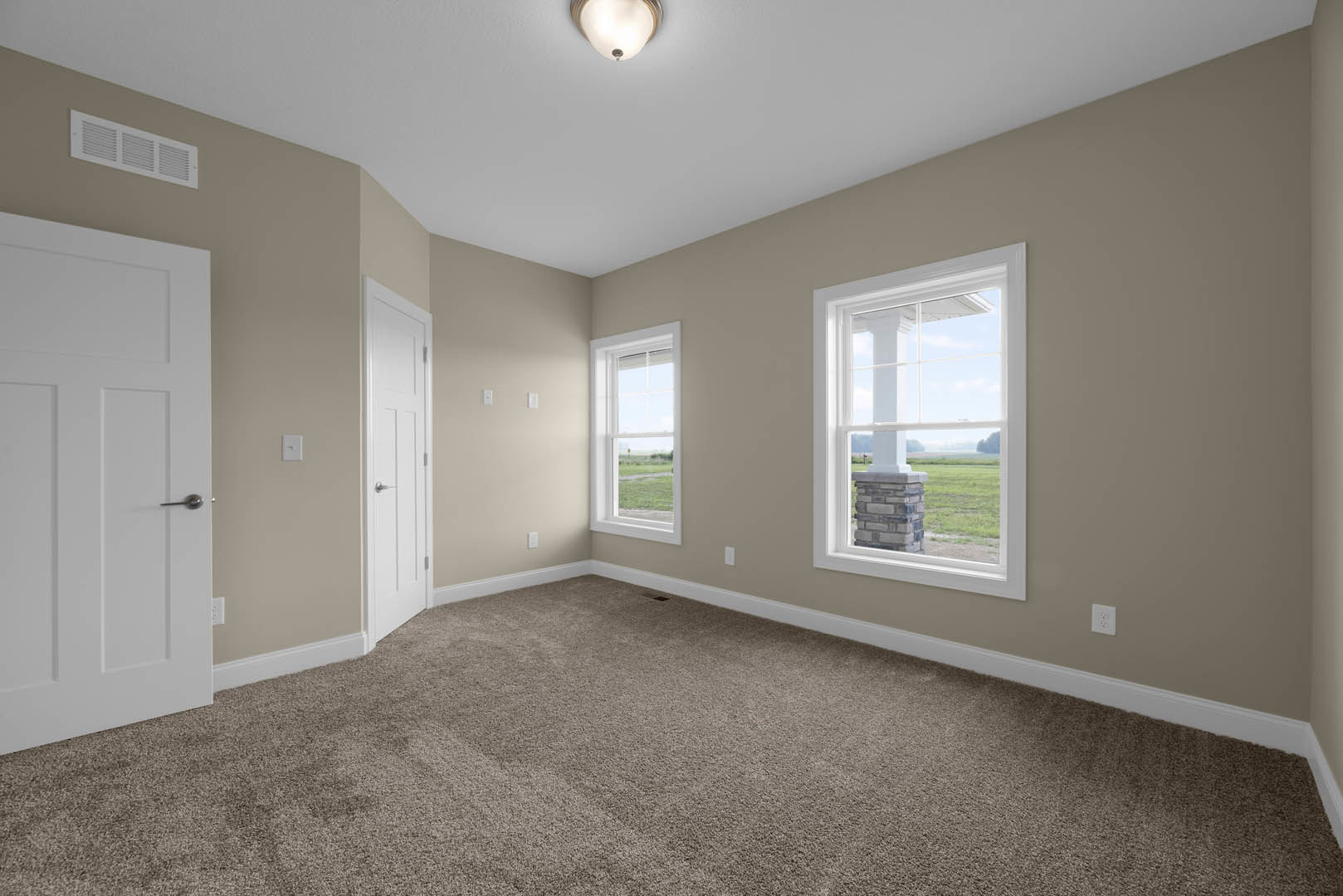 Carpeted room with large window framed by white molding, white walls, paneled door, and ceiling light fixture; window overlooks grassy field.