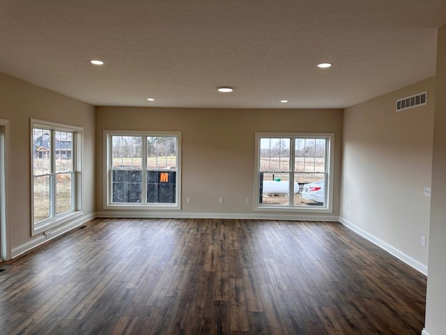 Wood flooring in a bright room with large windows, white walls, and a smooth ceiling