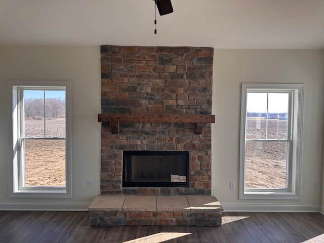 Stone fireplace with black fire screen, flanked by large windows, tile flooring, and neutral walls in a cozy den.